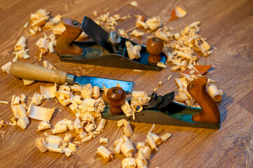 An old wooden jointer and a chisel with shavings lie on the wooden floor. Selective focus. 