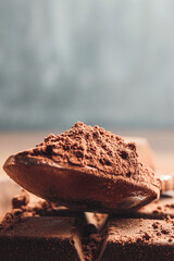 Brown cocoa powder in the spoon and chopped chocolate cubes, on dark background with copy space