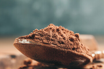 Brown cocoa powder in the spoon and chopped chocolate cubes, on dark background with copy space