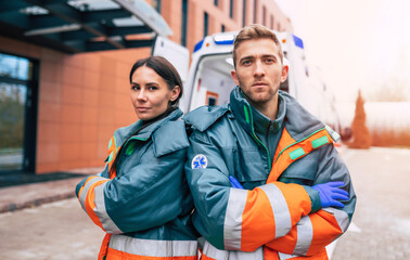 Two confident young doctors looking on the camera on ambulance and hospital background