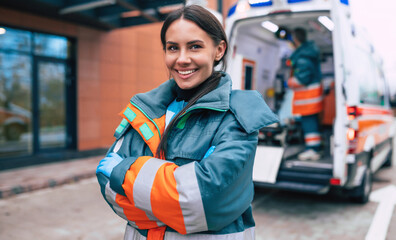 Professional and confident young woman doctor looking on the camera with ambulance background - obrazy, fototapety, plakaty