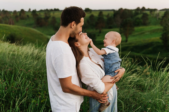 Young beautiful family with a little daughter hug, kiss and walk in nature. Photo of a family with a small child in nature.