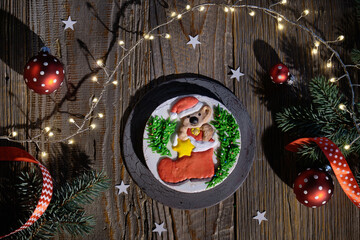 Ornate gingerbread decorated with bear character and Santa boot. Christmas flat lay with fir twigs, red baubles and festive lights. Dark wooden planks, top view of rustic table.