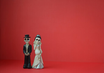 A close-up shot of two skeletons for Day of the Dead, Halloween, or Valentine's Day against a bright red background. Copy space
