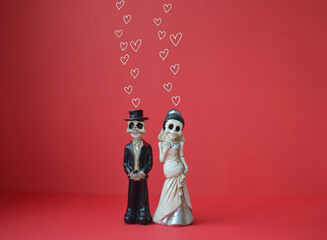 A close-up shot of two skeletons with hearts over their heads for Day of the Dead, Halloween, or Valentine's Day against a bright red background. Copy space