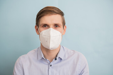 Man wearing FFP2 face mask while standing against blue background. Time to upgrade masks as coronavirus variants emerge. Double masking Covid-19 protection. FFP2 respirator for public health