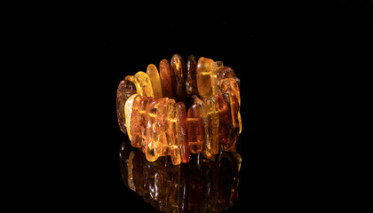 Glittering old orange Baltic amber bracelet on a black background. Isolated amber jewelry.