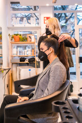 Caucasian hairdresser with mask giving the final touches to the brunette client's hairstyle. Security measures of Hairdressers in the Covid-19 pandemic