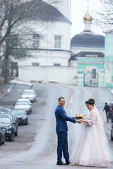 the bride and groom on the background of a church, religious lovers, a wedding walk in winter, a man and a woman gently kiss and smile hugs