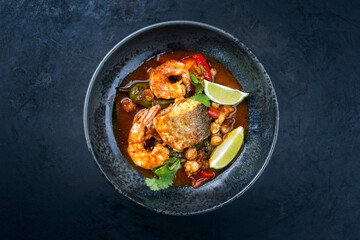 Modern style traditional Mexican seafood pozole soup with fish, king prawns and hominy in a clear sauce served as top view in design bowl