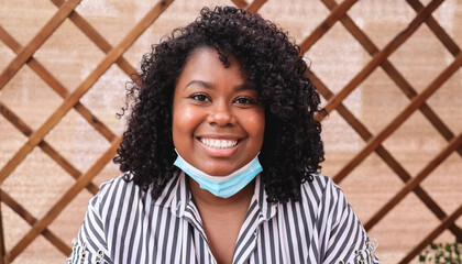 Young african woman smiling on camera with safety mask under chin - Focus on face