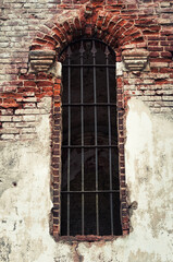 Fototapeta na wymiar Fragment of an ancient brick wall with a window with a lattice of a medieval church as texture or background
