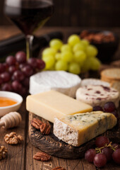 Glass of red wine with selection of various cheese and grapes on wooden background. Blue Stilton, Red Leicester and Brie Cheese and bowl of nuts and crackers. Top view