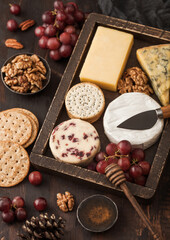 Selection of various cheese in vintage box grapes on wooden table background. Blue Stilton, Red Leicester and Brie Cheese and nuts with crackers and honey.
