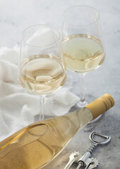 Bottle of white wine with two crystal glasses and steel corkscrew on light background.