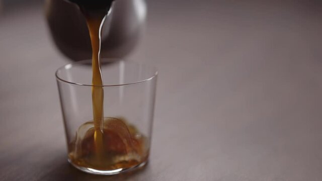 Slow motion coffee pour into tumbler glass on walnut table