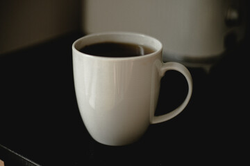 kawa, herbata w białym kubku, filiżance,  czarny blat, poranek, biało kubek na czarnym blacie