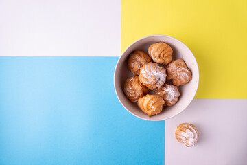 Choux pastry profiteroles on a yellow, blue, white background. View from above.