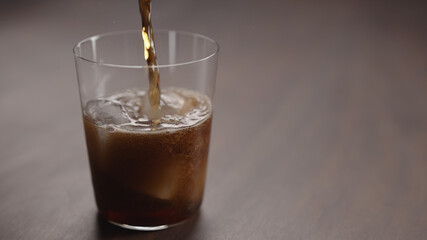pour cola over ice cubes into tumbler glass on walnut table with copy space