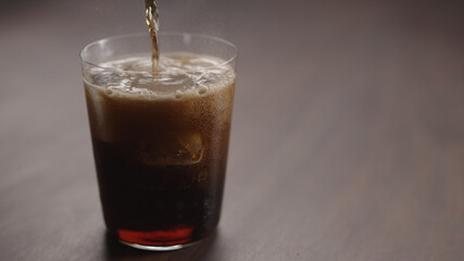 pour cola over ice cubes into tumbler glass on walnut table with copy space