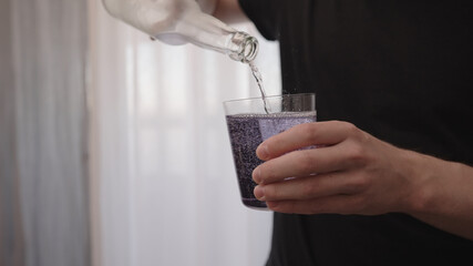 man pouring purple drink into tumbler glass near window