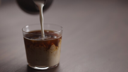 milk pour into tumbler glass with coffee on walnut table