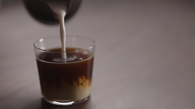 milk pour into tumbler glass with coffee on walnut table