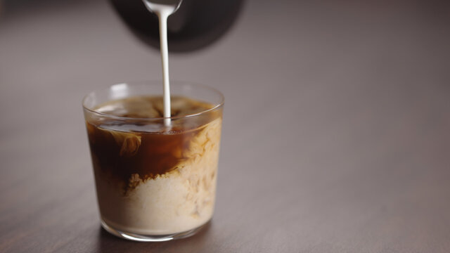 milk pour into tumbler glass with coffee on walnut table