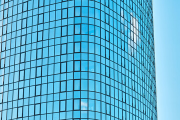 Stylish highrise office building with shiny blue glass facade reflecting bright sunlight against clear blue sky on sunny day