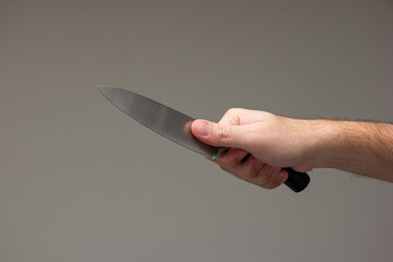 Caucasian male hand holding a large kitchen knife isolated on gray background