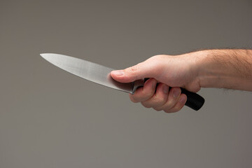 Caucasian male hand holding a large kitchen knife isolated on gray background