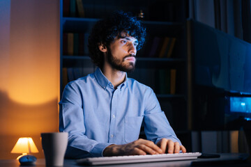 Close-up view of thoughtful young business man working on computer in home at night. Focused...