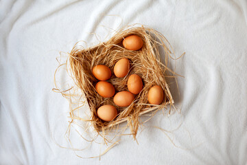 Painted Easter eggs lie on straw in a wooden box on a white soft blanket. Bright Easter holiday.