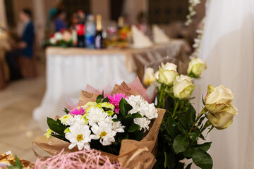 decorations with flowers at the wedding, the interior of the restaurant is prepared by the decorator for the holiday, beautiful fresh flowers in vases on the table, a bouquet as a gift from the guests