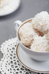 
Coconut candies close-up in a porcelain cup. Homemade Rafaello sweets in coconut flakes with almonds