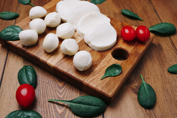 White small mozzarella cheese balls, spinach leaves and tomatoes on wooden board.