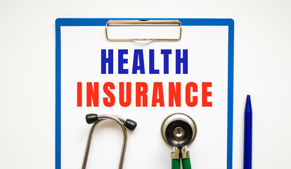 Clipboard with page and text HEALTH INSURANCE, on a table with a stethoscope and pen.