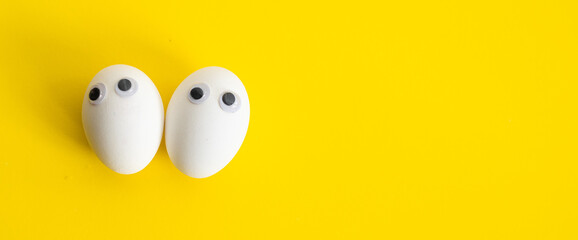 Banner two cute white eggs with eyes looks like two person. Faces of two people on yellow background top view. lovely couple.