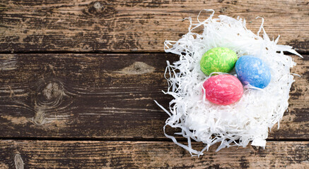 Three easter colors eggs are arranged on nest of white paper straw. Easter is  main event for believers, timed coincide with resurrection of Jesus Christ. Nest on wooden background. banner