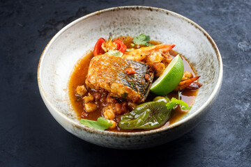 Modern style traditional Mexican seafood pozole soup with fish, king prawns and hominy in a clear sauce served as close-up in design bowl