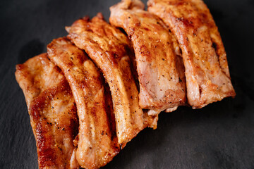 fried with spices pork ribs in a glass baking sheet on a stone black background. cooked meat at home. Barbecue.
