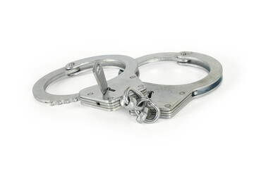 Handcuffs with key isolated on white background with light shadows. Pair of closed silver handcuffs macro close-up high resolution.