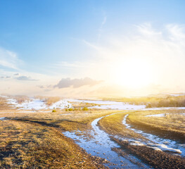 grass hill with melting snow at the sunset, spring outdoor evening scene