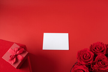 Red roses, red gift boxes and white card on red background