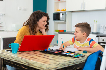Fototapeta na wymiar Smiling mother helping adorable son doing schoolwork at home