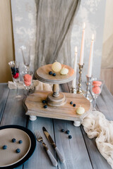 Candles on a cake stand with a wooden background. Table with glasses, plate, burning candles and cutlery. Elegant festive table setting and room decor.