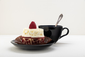Cake basket with cream and raspberries, on a black saucer with a cup of tea. on a light background