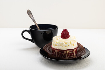 Cake basket with cream and raspberries, on a black saucer with a cup of tea. on a light background
