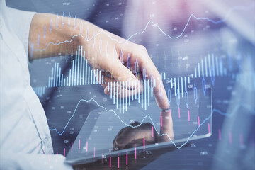 Double exposure of man's hands holding and using a digital device and forex graph drawing. Financial market concept.