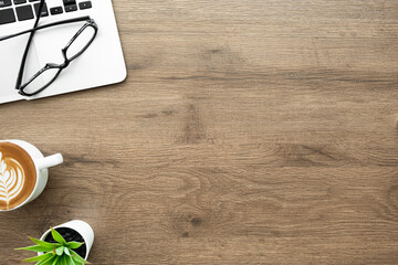 Wood office desk table with laptop computer, cup of latte coffee and supplies. Top view with copy space, flat lay.